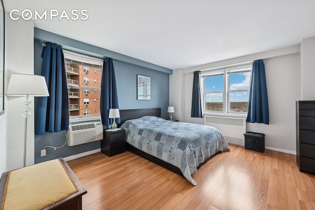 bedroom featuring wood finished floors, baseboards, cooling unit, and radiator