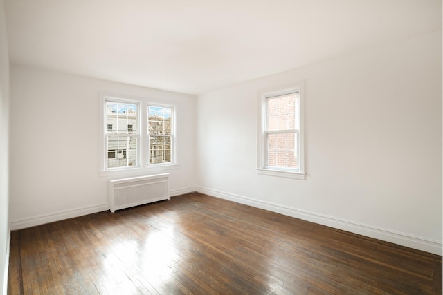 unfurnished room featuring dark wood-type flooring, baseboards, radiator, and a healthy amount of sunlight