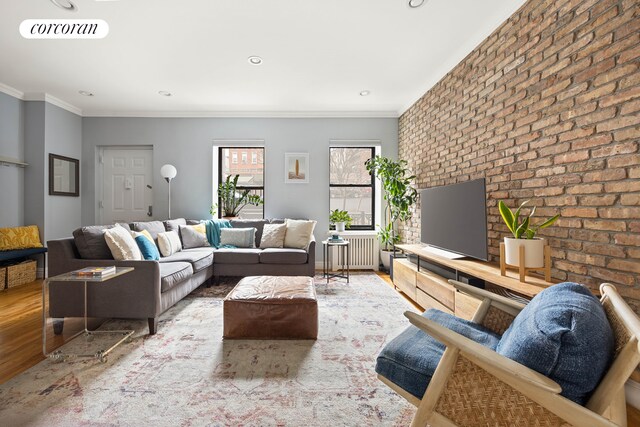 living area with wood finished floors, brick wall, ornamental molding, radiator, and recessed lighting
