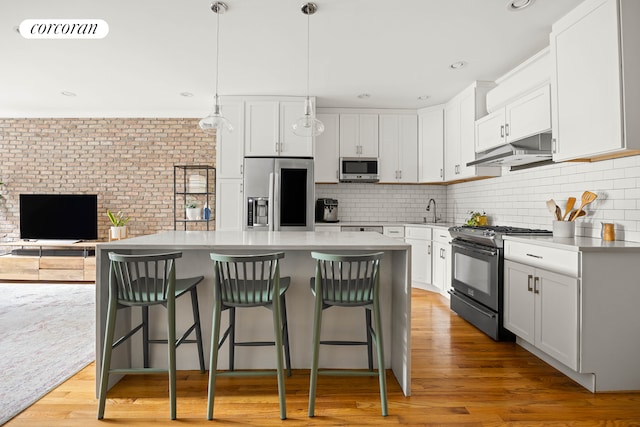 kitchen featuring appliances with stainless steel finishes, a sink, under cabinet range hood, white cabinets, and brick wall