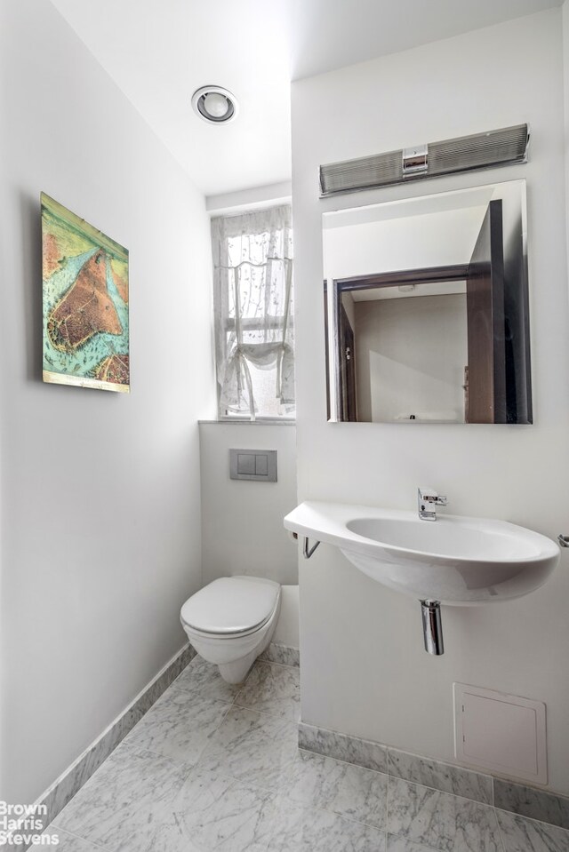 345 E 57th St Unit 8Ab, New York City, NY 10022 - bathroom featuring toilet, baseboards, marble finish flooring, and a sink