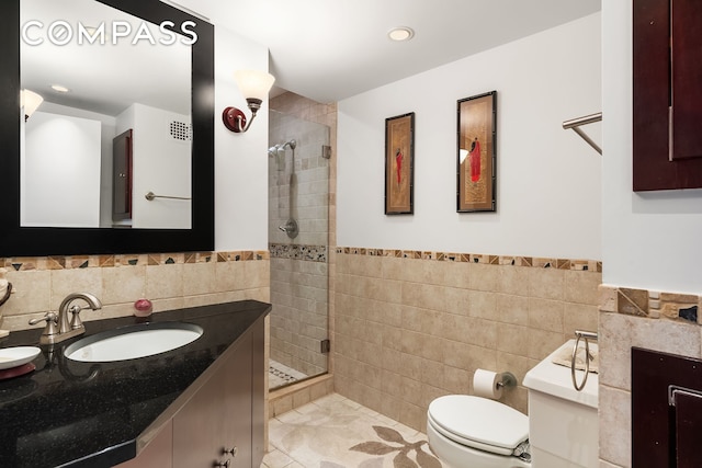 bathroom with tile walls, a stall shower, a wainscoted wall, vanity, and toilet