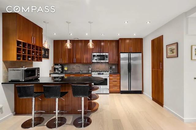 kitchen with appliances with stainless steel finishes, a peninsula, dark countertops, backsplash, and recessed lighting