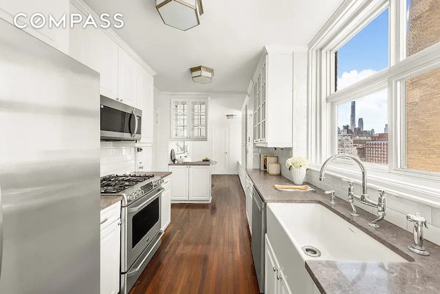 kitchen with appliances with stainless steel finishes, a sink, white cabinetry, backsplash, and glass insert cabinets