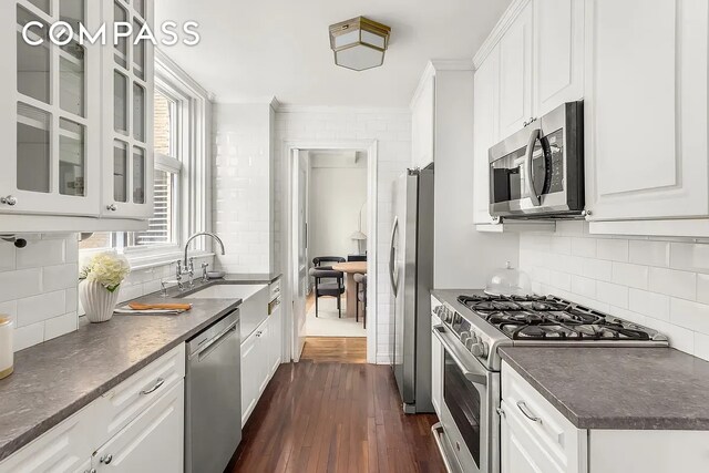 kitchen with dark countertops, a sink, stainless steel appliances, white cabinetry, and dark wood-type flooring