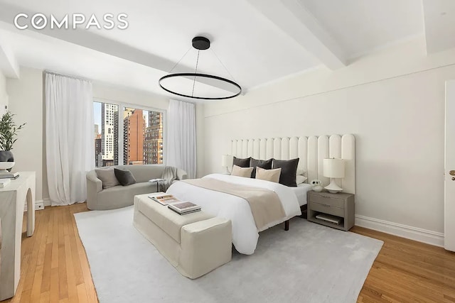 bedroom featuring light wood-type flooring, baseboards, and beam ceiling