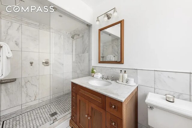 full bathroom featuring vanity, tile walls, a stall shower, and toilet