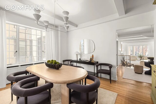 dining area featuring beamed ceiling, an inviting chandelier, and light wood-style flooring