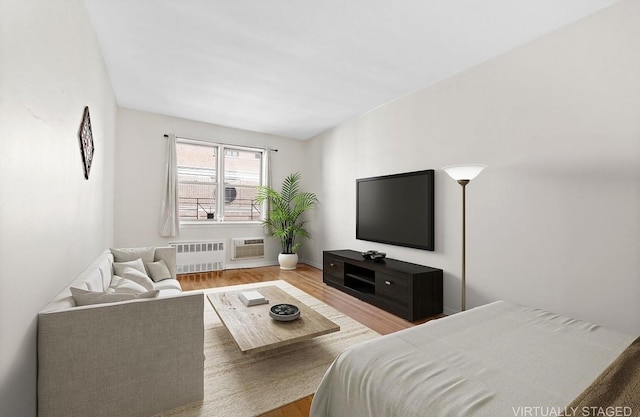living area featuring radiator heating unit, wood finished floors, a wall mounted AC, and baseboards