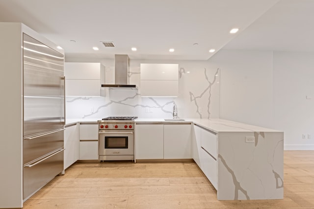 kitchen with premium appliances, wall chimney exhaust hood, white cabinets, a sink, and recessed lighting