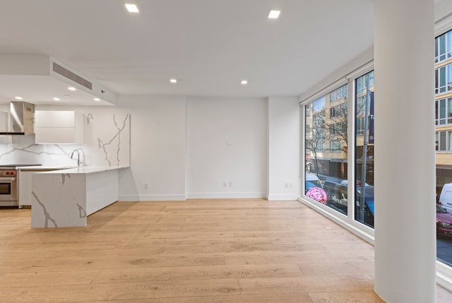 kitchen with high end range, light wood-style flooring, recessed lighting, white cabinets, and wall chimney range hood