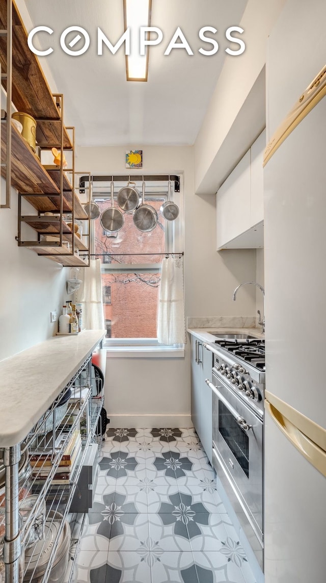 400 E 59th St Unit 3G, New York City, NY 10022 - kitchen with freestanding refrigerator, high end stove, white cabinets, baseboards, and a sink