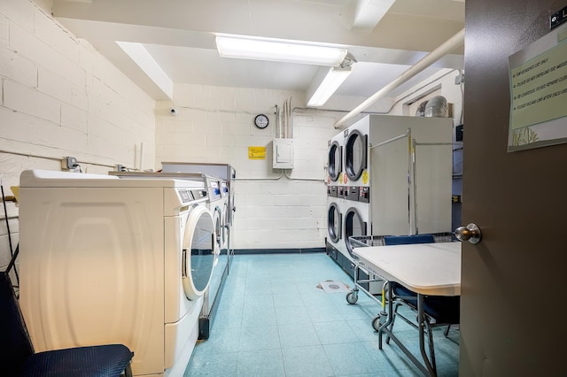 community laundry room with concrete block wall, stacked washer / drying machine, washing machine and dryer, and tile patterned floors