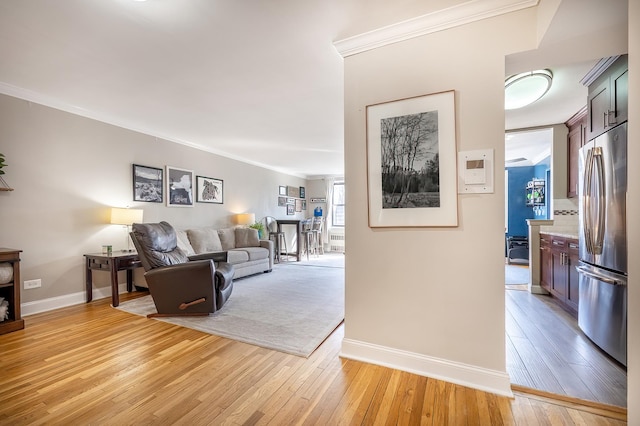living area with baseboards, ornamental molding, and light wood finished floors