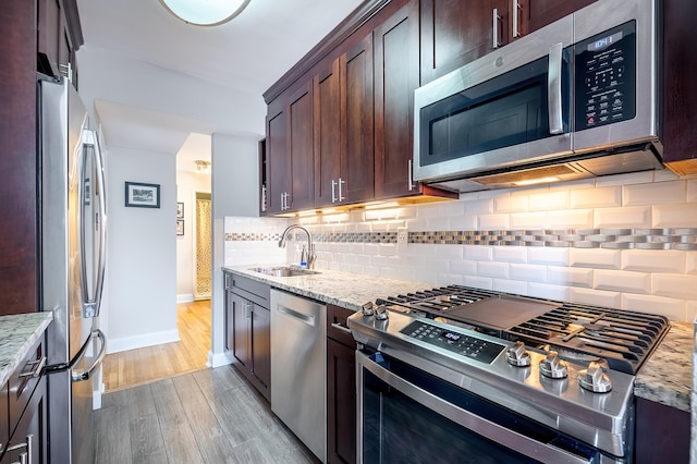 kitchen with decorative backsplash, light stone countertops, light wood-style floors, a sink, and appliances with stainless steel finishes
