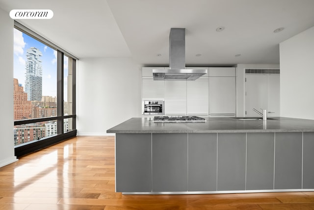 101 Warren St Unit 1720, New York City, NY 10007 - kitchen featuring island exhaust hood, stainless steel appliances, modern cabinets, white cabinets, and light wood-type flooring