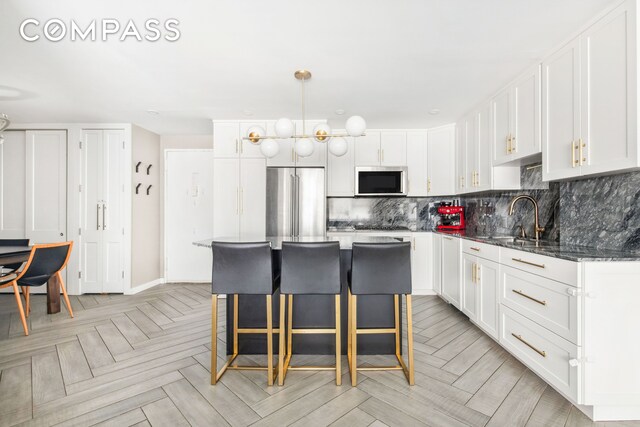 340 E 80th St Unit 1D, New York City, NY 10075 - kitchen with stainless steel appliances, white cabinetry, a kitchen breakfast bar, decorative backsplash, and a center island