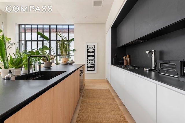 bar featuring a sink, visible vents, a toaster, light wood finished floors, and stainless steel gas cooktop