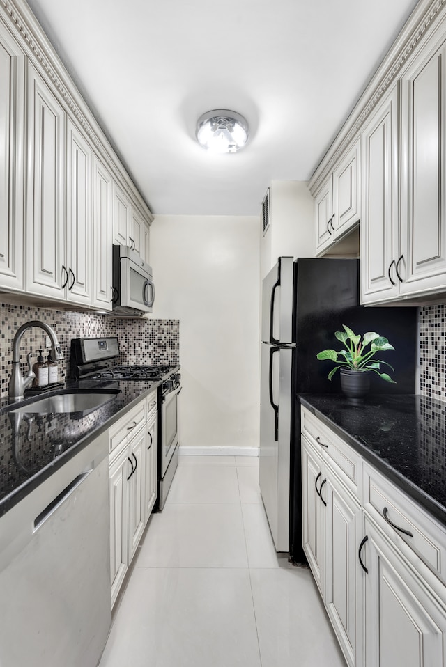 kitchen featuring light tile patterned floors, tasteful backsplash, appliances with stainless steel finishes, a sink, and baseboards