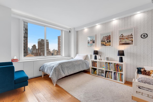 bedroom featuring recessed lighting, wallpapered walls, a city view, and wood finished floors