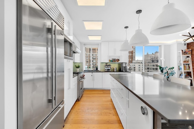 kitchen featuring high quality appliances, dark countertops, hanging light fixtures, light wood-style floors, and white cabinetry