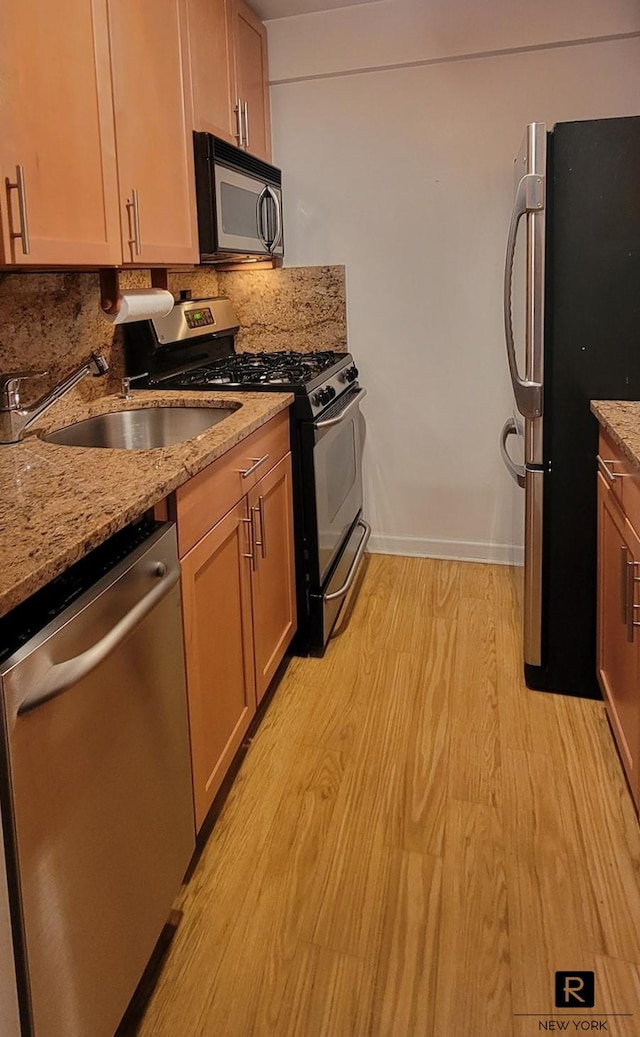 kitchen with light stone countertops, baseboards, light wood finished floors, appliances with stainless steel finishes, and backsplash