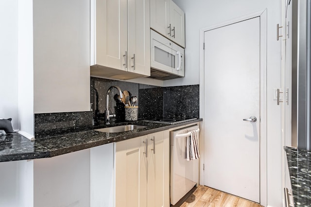 kitchen featuring decorative backsplash, white microwave, a sink, dark stone countertops, and dishwasher
