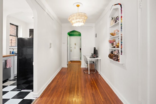 hall featuring baseboards, arched walkways, a chandelier, and wood finished floors