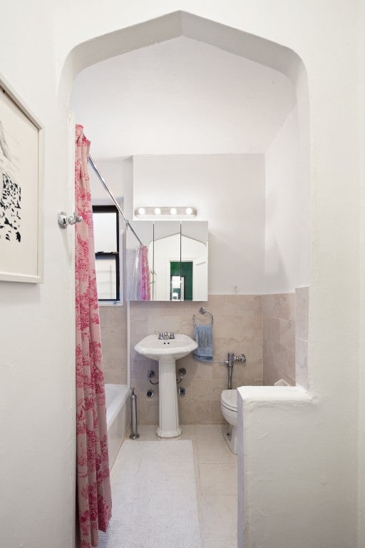 full bathroom with shower / bath combination with curtain, tile patterned flooring, toilet, a sink, and tile walls