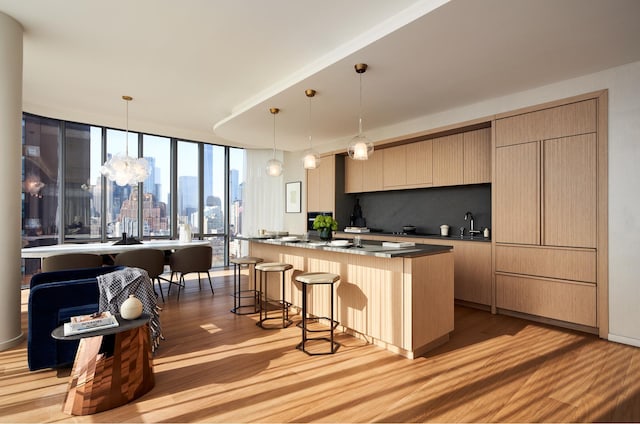 kitchen with tasteful backsplash, an island with sink, a breakfast bar, dark countertops, and light wood finished floors