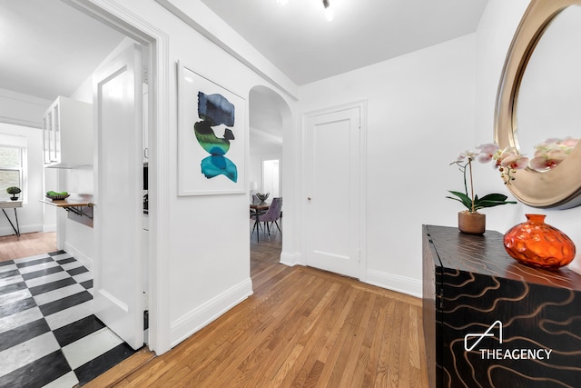 corridor featuring arched walkways, light wood-type flooring, and baseboards