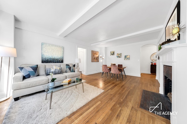 living area with beam ceiling, arched walkways, hardwood / wood-style floors, a fireplace, and baseboards