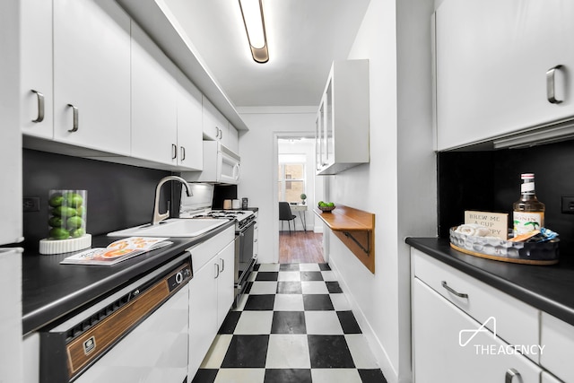 kitchen featuring white appliances, dark floors, white cabinetry, a sink, and dark countertops