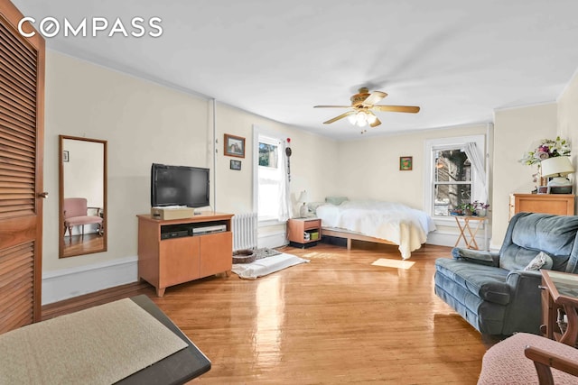 bedroom featuring light wood-type flooring, radiator, a ceiling fan, and baseboards