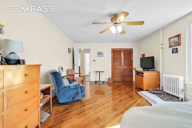 bedroom featuring radiator, light wood-style floors, crown molding, ceiling fan, and a closet