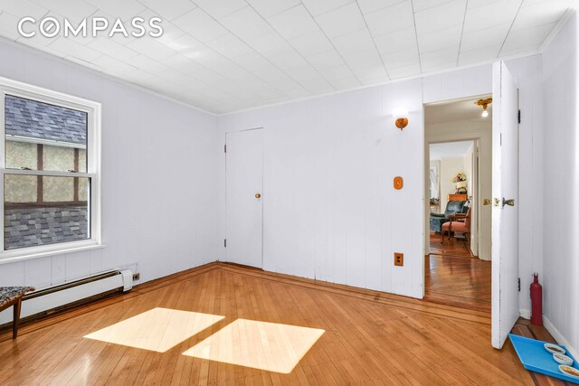 unfurnished room with a baseboard heating unit, wood-type flooring, and ornamental molding
