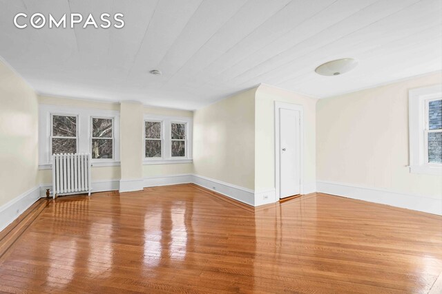 spare room with radiator, wood finished floors, and baseboards