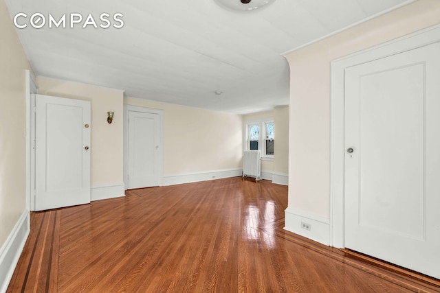 unfurnished living room featuring radiator, wood finished floors, and baseboards