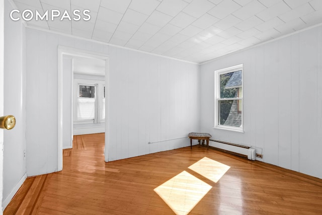 unfurnished room featuring a baseboard heating unit, crown molding, and hardwood / wood-style floors
