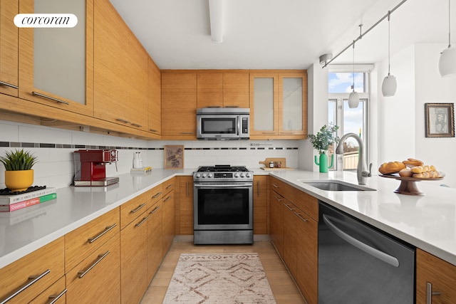kitchen with appliances with stainless steel finishes, a sink, backsplash, light countertops, and brown cabinetry