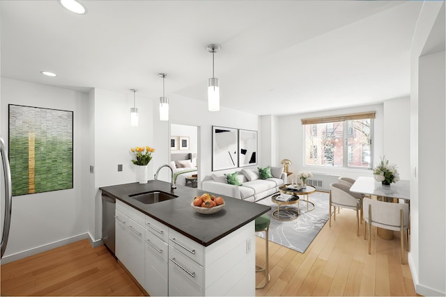 kitchen featuring stainless steel dishwasher, light wood-style floors, dark countertops, a sink, and a peninsula