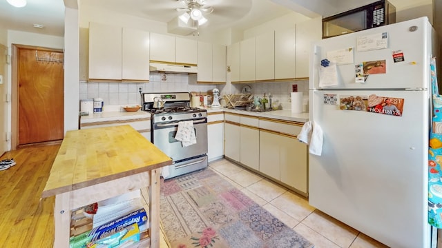 kitchen featuring black microwave, stainless steel range with gas stovetop, freestanding refrigerator, wood counters, and under cabinet range hood