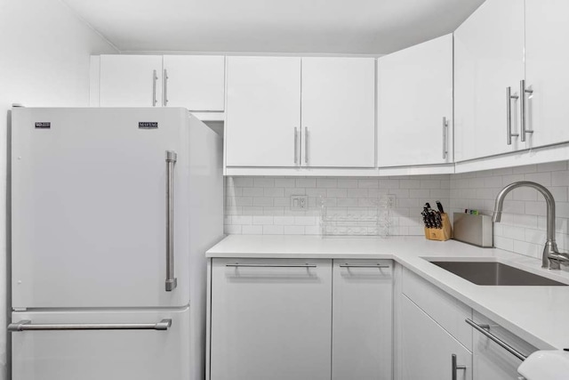 kitchen featuring freestanding refrigerator, light countertops, white cabinetry, a sink, and backsplash