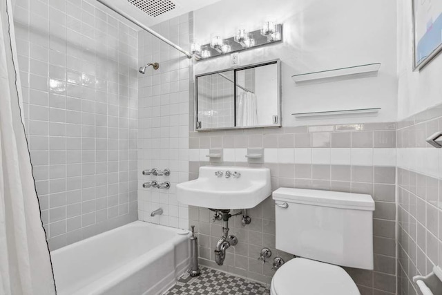 full bathroom featuring toilet, tile walls, shower / bathtub combination with curtain, tile patterned floors, and a sink