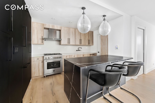 kitchen with light brown cabinets, wall chimney exhaust hood, high end range, light wood-type flooring, and a kitchen bar