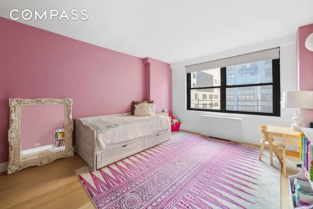 bedroom featuring baseboards, wood finished floors, and radiator heating unit