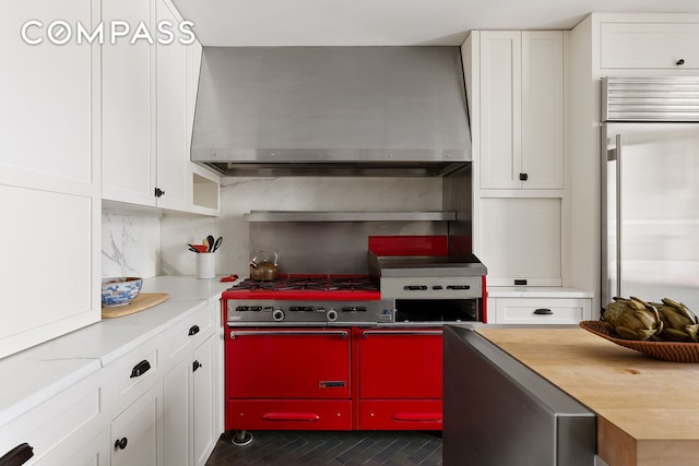 kitchen featuring wall chimney exhaust hood, premium appliances, decorative backsplash, and white cabinets