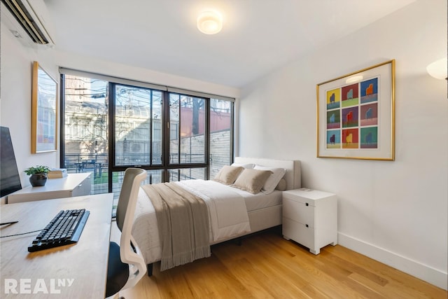 143 Meserole St Unit 1A, New York City, NY 11206 - bedroom with a wall mounted air conditioner, light wood-style floors, and baseboards