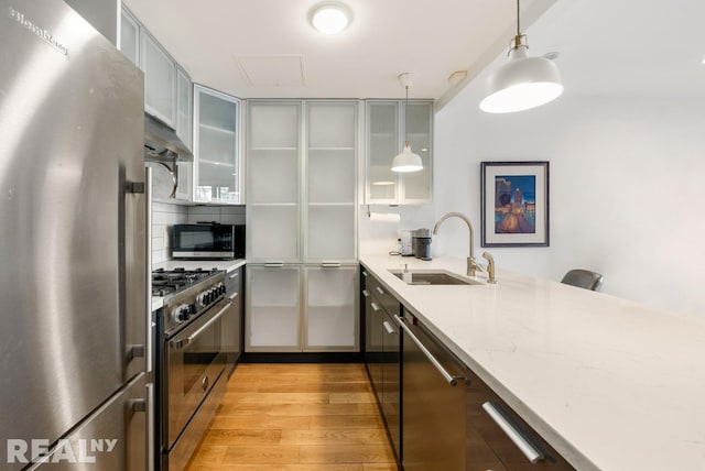 143 Meserole St Unit 1A, New York City, NY 11206 - kitchen featuring appliances with stainless steel finishes, a sink, hanging light fixtures, light wood finished floors, and light stone countertops