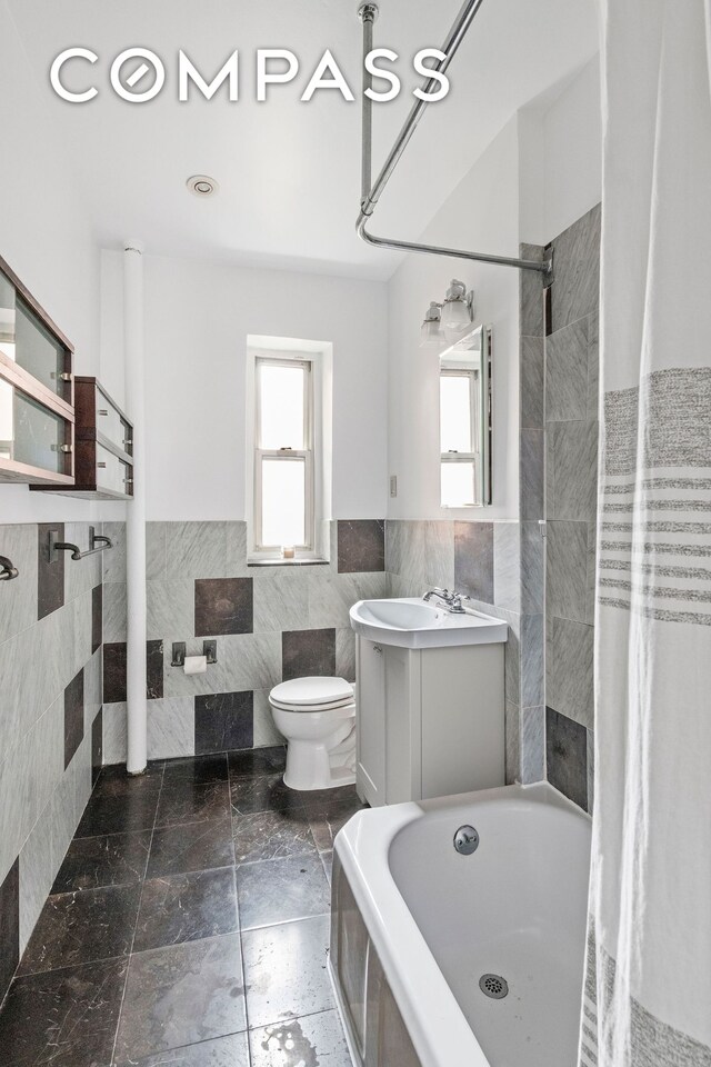 525 E 89th St Unit 3A, New York City, NY 10128 - bathroom featuring tile walls, plenty of natural light, wainscoting, toilet, and a bath